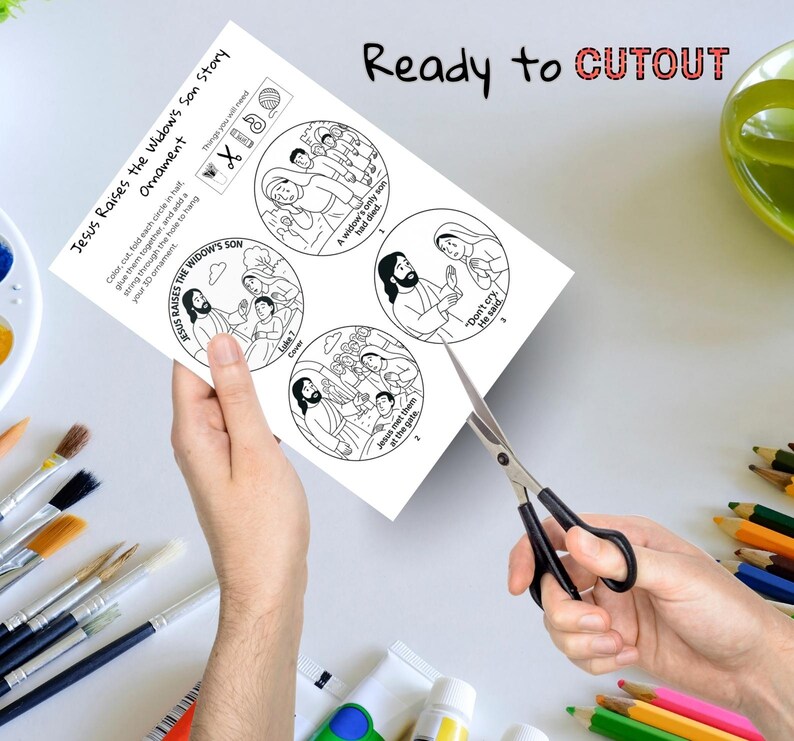 May include: A black and white paper craft with the text "Jesus Raises the Widow's Son Story" and "Ready to CUTOUT". The paper has four circular illustrations and instructions. A pair of scissors is cutting the paper.