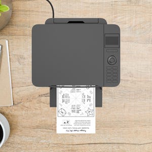 May include: A gray printer is printing a white sheet of paper with a fortune teller design. The paper has the text "Prayer Model FACTS" at the bottom. The printer is on a light brown wooden surface, with a pen, notepad, and coffee cup visible.