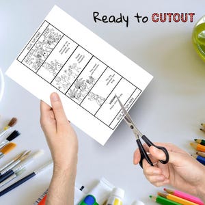 May include: A white paper with a black and white illustrated story is being cut with scissors. The text "Ready to CUTOUT" is written in black and red. The paper has the text "GLUE TOP HERE" and "GLUE BOTTOM HERE".