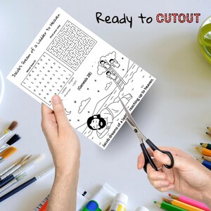 May include: A black and white activity sheet titled "Jacob's Dream of a Ladder to Heaven" is being cut with scissors. The sheet includes a word search, a maze, and an illustration of a ladder reaching up to heaven. The text "Ready to CUTOUT" is at the top.