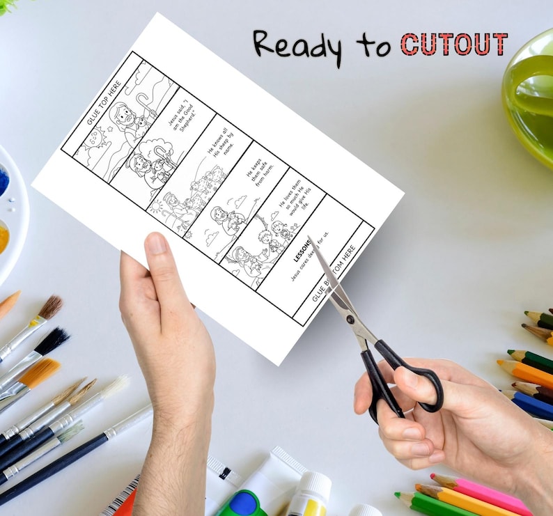May include: A white paper with a black and white illustrated story about Jesus and his sheep. The text "Ready to CUTOUT" is written in black and red. Scissors are cutting the paper. Paintbrushes and colored pencils are in the background.