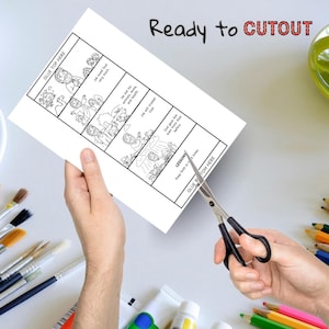 Pu&ograve; includere: Un foglio di carta bianco con una storia illustrata in bianco e nero su Giobbe, con la scritta "Ready to CUTOUT". La carta viene tagliata con le forbici. Pennelli, vernice e matite colorate sono sullo sfondo.