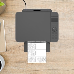 May include: A grey printer on a wooden desk, printing a sheet with four black and white cartoon illustrations. A pen, notepad, and coffee cup are also visible. The image is taken from above.