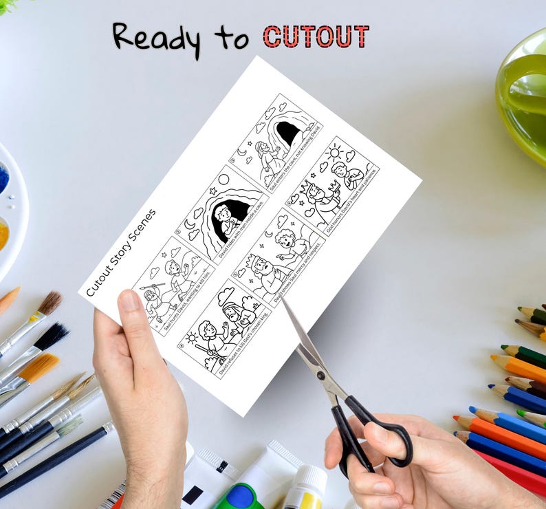 May include: A person's hands are holding a white sheet of paper with black and white illustrations and text, and cutting it with scissors. The text on the paper says "Cutout Story Scenes" and "Ready to CUTOUT".