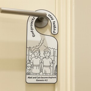 May include: A white door hanger with a black outline, featuring an illustration of two people and a sheep, with the text "Abel and Cain become shepherds Genesis 4:2". The top has the words "God protects, stay faithful".