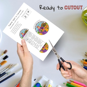 May include: A white paper craft activity sheet titled "Twelve Spies in Canaan" with a colorful illustration. The sheet includes instructions and a story wheel design. Scissors are cutting the paper, with the text "Ready to CUTOUT" at the top.