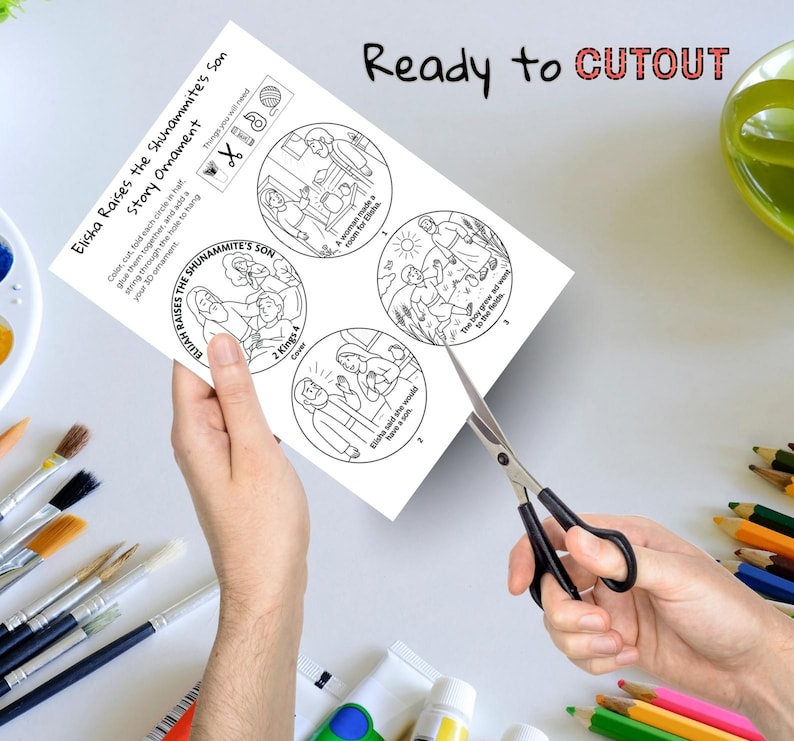 May include: A white paper with a black and white illustration of a Bible story, titled "Elisha Raises the Shunammite's Son Story Ornament." The text "Ready to CUTOUT" is at the top. Scissors are cutting the paper.
