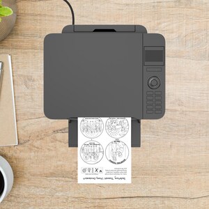 May include: A gray printer is printing a sheet of paper with four circular illustrations and text. The text reads "Doubting Thomas Story Ornament". The printer is on a light brown wooden surface.