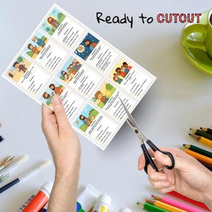 May include: A sheet of illustrated cards with religious themes is being cut with scissors. The cards feature cartoon images and text, with the words "Ready to Cutout" at the top. A green mug and art supplies are in the background.