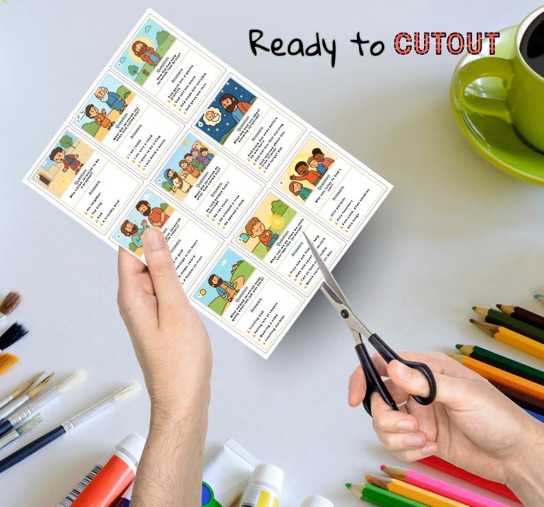 May include: A sheet of illustrated cards with religious themes is being cut with scissors. The cards feature cartoon images and text, with the words "Ready to Cutout" at the top. A green mug and art supplies are in the background.