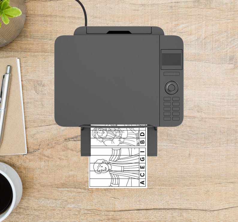 May include: A grey printer printing a black and white illustration of two figures with the letters ACEGIBD. The printer is on a light brown wooden surface, with a pen, notepad, and a cup of coffee visible.