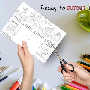 May include: A person is cutting out a black and white illustrated children's activity sheet with scissors. The sheet features Bible story panels with text: "Elijah & the Ravens" and "Ready to CUTOUT". A green mug and colored pencils are in the background.