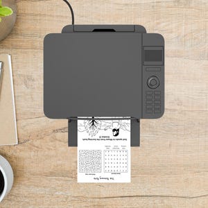 May include: A gray printer is printing a black and white activity sheet with a maze and a drawing of a burning bush. The text on the sheet reads "God speaks to Moses from the burning bush" and "The Burning Bush."