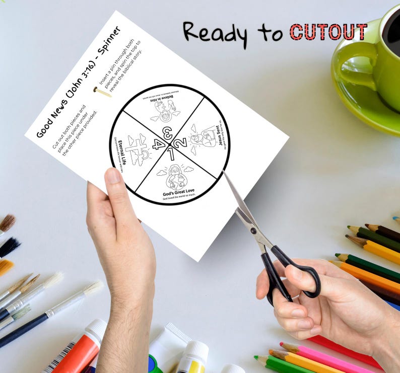May include: A white paper spinner with the text "Good News (John 3:16) - Spinner" is being cut with scissors. The spinner has a circular design with illustrations and the words "Eternal Life", "Believe in Him", "Jesus Sent", and "God's Great Love". The words "Ready to CUTOUT" are written at the top.