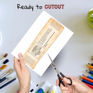 May include: A white paper with a scroll design is being cut with scissors. The scroll has text and a small illustration. The words "Ready to CUTOUT" are at the top. Paint tubes, brushes, and colored pencils are in the background.
