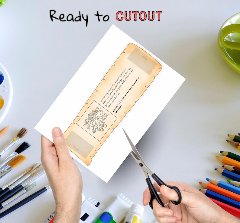 May include: A white paper with a scroll design is being cut with scissors. The scroll has text and a small illustration. The words "Ready to CUTOUT" are at the top. Paint tubes, brushes, and colored pencils are in the background.