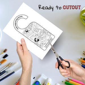 May include: A black and white door hanger with a biblical illustration, being cut with scissors. The text "Ready to CUTOUT" is above the door hanger. The door hanger has the text "Faith helps bring miracle" and "Friends bring a paralyzed man to Jesus for healing."