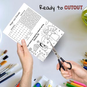 May include: A black and white activity sheet with a word search and illustration is being cut out with scissors. The text on the sheet reads "Hagar and Ishmael" and "Ready to CUTOUT". The illustration depicts an angel and a woman.