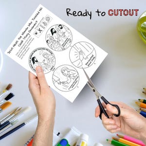 May include: A black and white illustrated paper craft titled "Jesus Heals the Woman Who Touched His Cloak Story Ornament." The paper has four circular illustrations and the text "Ready to CUTOUT." Scissors are cutting the paper.