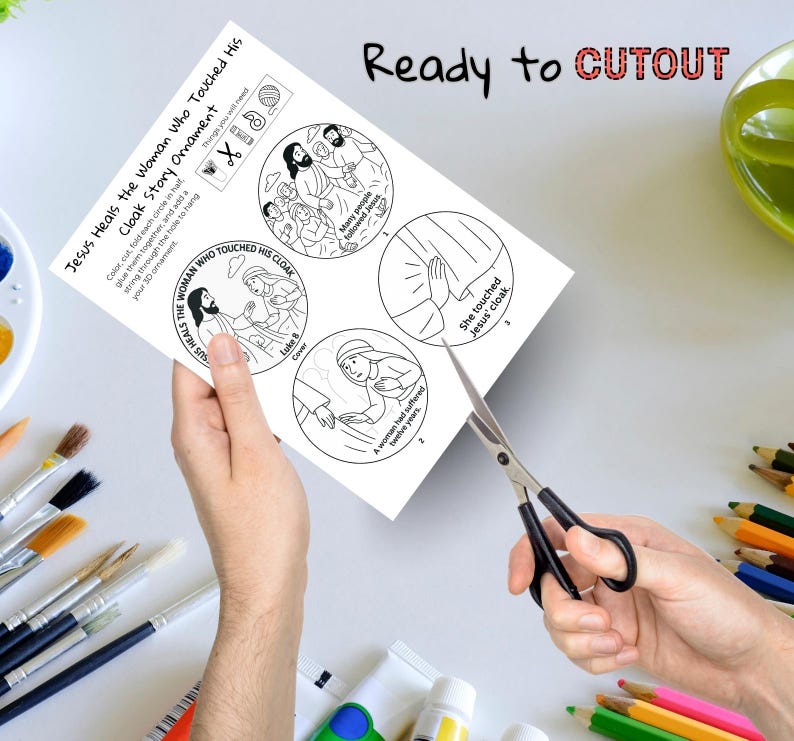May include: A black and white illustrated paper craft titled "Jesus Heals the Woman Who Touched His Cloak Story Ornament." The paper has four circular illustrations and the text "Ready to CUTOUT." Scissors are cutting the paper.