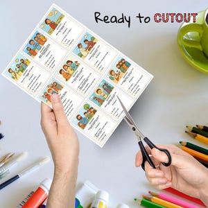 May include: A sheet of printed cards with illustrations and text, held by a person's hands, being cut with scissors. The cards feature colorful drawings of people and scenes, with questions and answers. The text "Ready to CUTOUT" is visible.