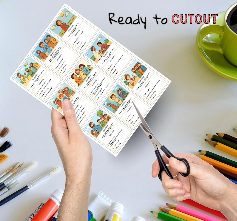 May include: A sheet of printed cards with illustrations and text, held by a person's hands, being cut with scissors. The cards feature colorful drawings of people and scenes, with questions and answers. The text "Ready to CUTOUT" is visible.