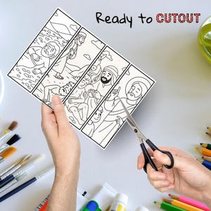 Pu&ograve; includere: Un fumetto illustrato in bianco e nero raffigurante figure religiose, con la scritta "Ready to CUTOUT" in nero e rosso. Un paio di forbici sta tagliando la carta. Pennelli, tubetti di vernice e matite colorate sono sullo sfondo.