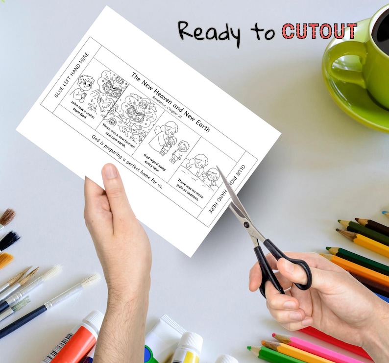 May include: A black and white illustrated paper with the text "The New Heaven and New Earth" is being cut with scissors. The paper has illustrations and text, including "Ready to CUTOUT". A green mug and colored pencils are in the background.