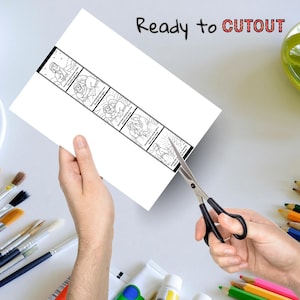 May include: A white sheet of paper with a black and white comic strip is being cut with scissors. The text "Ready to CUTOUT" is written at the top. Paintbrushes, paint tubes, and colored pencils are in the background.