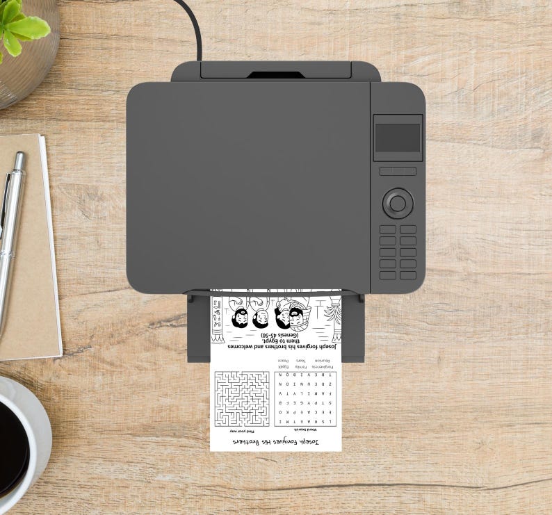 May include: A grey printer producing a black and white activity sheet. The sheet features the text "Joseph Forgives His Brothers", a maze, and an illustration. The printer sits on a wooden surface.