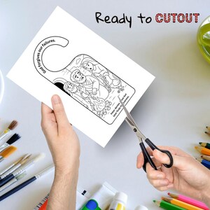 May include: A black and white door hanger with a biblical scene illustration is being cut out with scissors. The text "God forgives our failures" and "Ready to CUTOUT" are visible. The image also includes text that reads "Peter denies sus but later finds forgiveness."