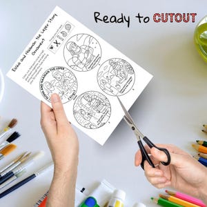 May include: A sheet of paper with a black and white illustration of the story of Elisha and Naaman the Leper. Scissors are being used to cut out the illustrations. The text "Ready to CUTOUT" is visible.