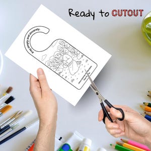 May include: A white door hanger with a black and white illustration of Jesus teaching disciples. The text "Pray simply and sincerely" and "Ready to CUTOUT" are printed on the door hanger. Scissors are cutting the door hanger.