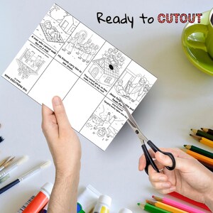 May include: A black and white illustrated cutout sheet with Bible story panels, including text like "The Paralyzed Man" and "Ready to CUTOUT." The sheet is being cut with scissors. Colored pencils and a green mug are in the background.