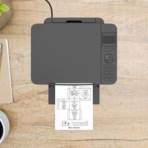 May include: A gray printer is printing a white sheet of paper with a diagram for a Vintage Cube. The printer is on a wooden surface, with a pen, notepad, and a cup of coffee visible.