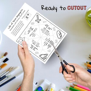 Op de afbeelding: Handen houden een wit papier met een zwart-wit illustratie van een kriebelverzamelaar. De tekst op het papier luidt "Life of Jesus (Highlights)" en "Ready to CUTOUT". Een schaar knipt het papier.