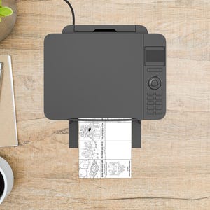 May include: Overhead view of a gray printer printing a black and white image. The printed image is a four-panel cartoon with text. The printer is on a light brown wooden surface, with a pen, notepad, and coffee cup visible.