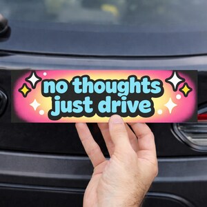 May include: A rectangular bumper sticker with the text "no thoughts just drive" in a playful font. The sticker has a black background with a gradient of pink, yellow, and orange. Decorative stars and sparkles surround the text.