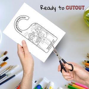 Puede incluir: Un colgador de puerta blanco con una ilustraci&oacute;n en blanco y negro de una escena b&iacute;blica se est&aacute; recortando con unas tijeras. El texto "Ready to CUTOUT" est&aacute; encima de la ilustraci&oacute;n. El colgador de puerta tiene el texto "Peacemaking brings God's favor."