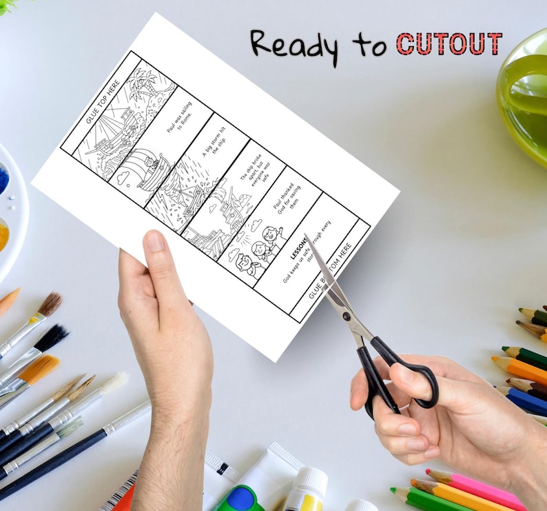 May include: A white paper with a black and white illustrated story about a ship, with the text "Ready to CUTOUT". Scissors are cutting the paper. Paintbrushes and colored pencils are in the background.