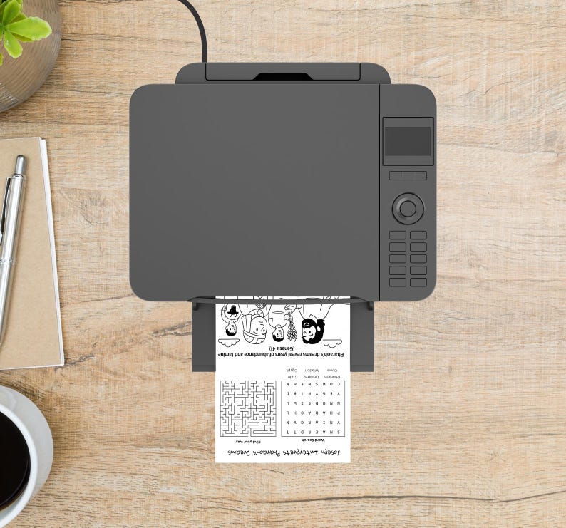 May include: A gray printer is printing a black and white page with illustrations and text. The page includes a maze and the text "Joseph Interprets Pharaoh's Dreams". The printer is on a light brown wooden surface.