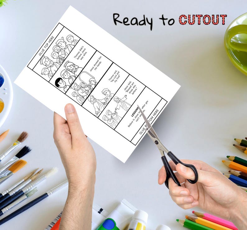 May include: A white paper with a black and white illustrated story, being cut with scissors. The paper has text that reads "Ready to CUTOUT" and "GLUE TOP HERE" and "GLUE BOTTOM HERE".