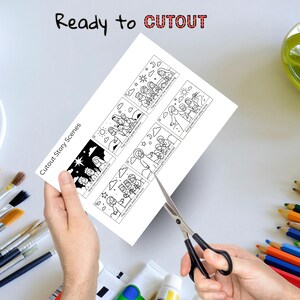 May include: A white sheet of paper titled Cutout Story Scenes featuring six black and white line art illustrations depicting the nativity story with text captions. The paper is being cut with black metal scissors, surrounded by various art supplies.