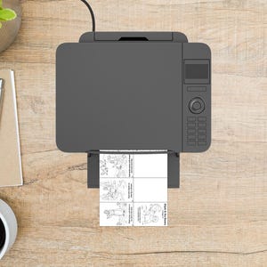 May include: Overhead view of a gray printer with a printed sheet of paper. The paper has four black and white illustrations with text. The printer is on a light brown wooden surface.