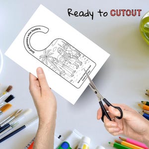 May include: A white door hanger with a black and white biblical illustration is being cut out with scissors. The text "Ready to CUTOUT" is at the top. The door hanger has text that reads "God empowers wise leaders" and "God raises Deborah to lead Israel to victory."