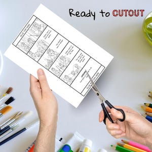 Peut inclure: Une feuille de papier blanche avec une histoire illustr&eacute;e en noir et blanc sur Esther, avec le texte "Ready to CUTOUT" en noir et rouge. Des ciseaux coupent le papier, avec des fournitures d'art en arri&egrave;re-plan.
