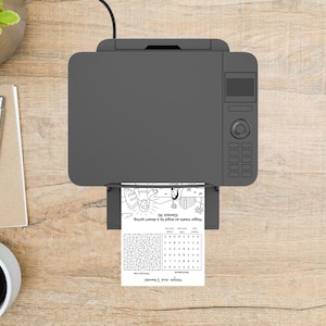 May include: A gray printer is printing a black and white activity sheet with a maze and text that reads "Hagar meets an angel by a desert spring (Genesis 16)" and "Hagar and Ishmael!" on a wooden surface.