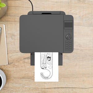 Op de afbeelding: Een bovenaanzicht van een grijze printer met een bedrukte bladwijzer. De bladwijzer is wit met een zwart-wit illustratie van mensen en de tekst "Stand firm in truth."