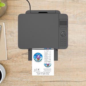 May include: A gray printer with a printed sheet of paper. The paper has a blue and purple graphic with the text "Jesus walks on water". The printer is on a light brown wooden surface.