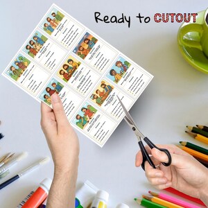 May include: A sheet of illustrated cards with questions and answers, held by a person's hands, with scissors cutting the cards. The text "Ready to CUTOUT" is printed at the top. A green mug and art supplies are in the background.
